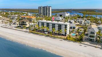 A beachfront hotel with a central building, a pool, and a beach view.