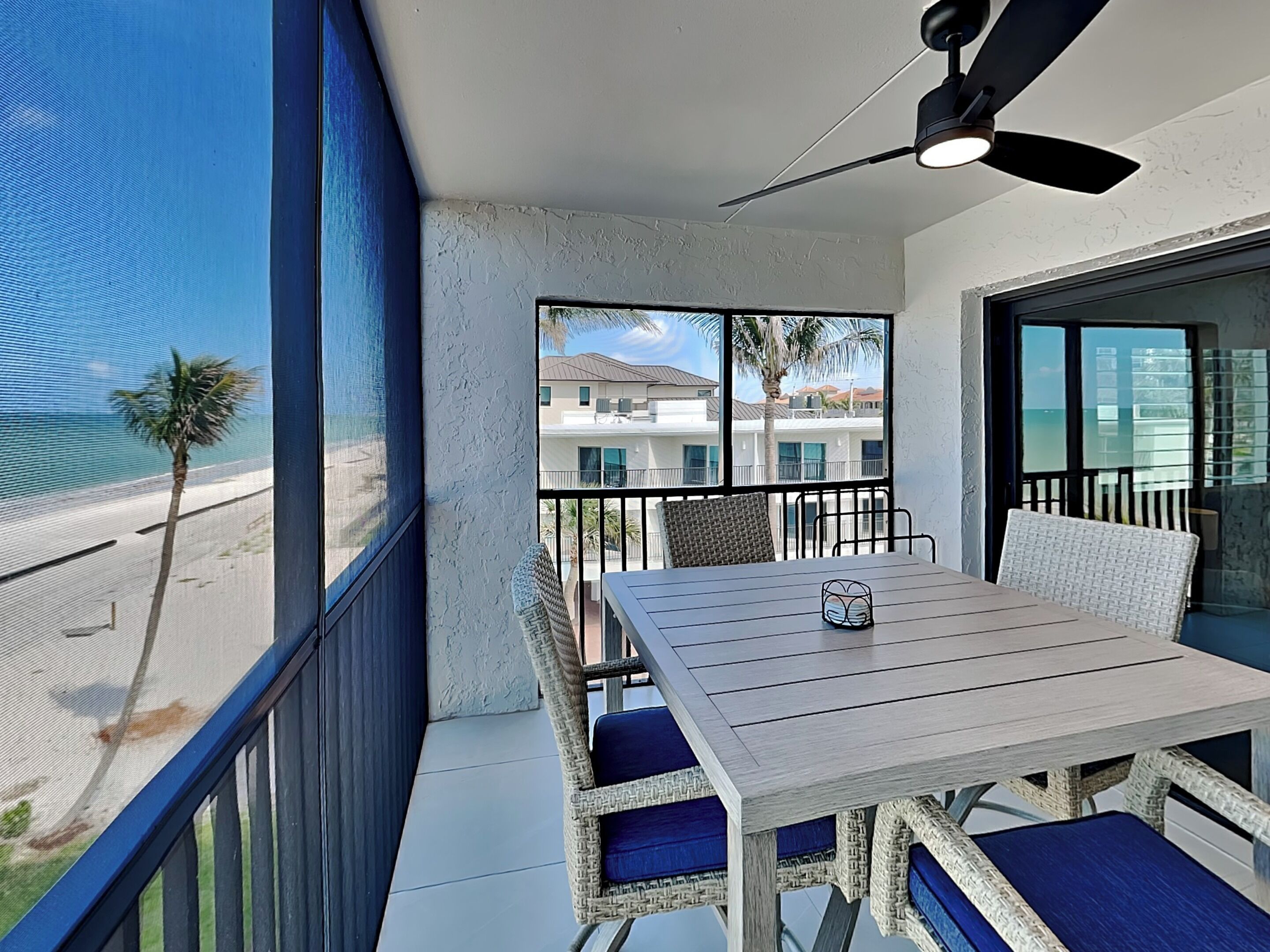 Un balcon avec une table et des chaises, donnant sur une plage et un immeuble.