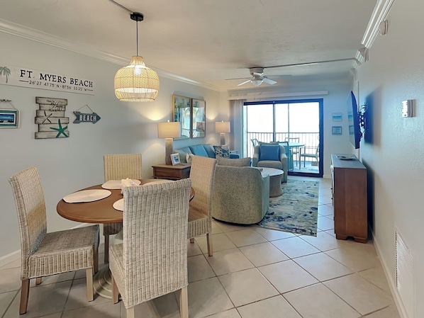 A dining area with wicker chairs and a round table, a living room with a sofa and armchairs, and a balcony with a view. - Seaside 3 by Distinctive Beach Rentals (Fort Myers Beach)
