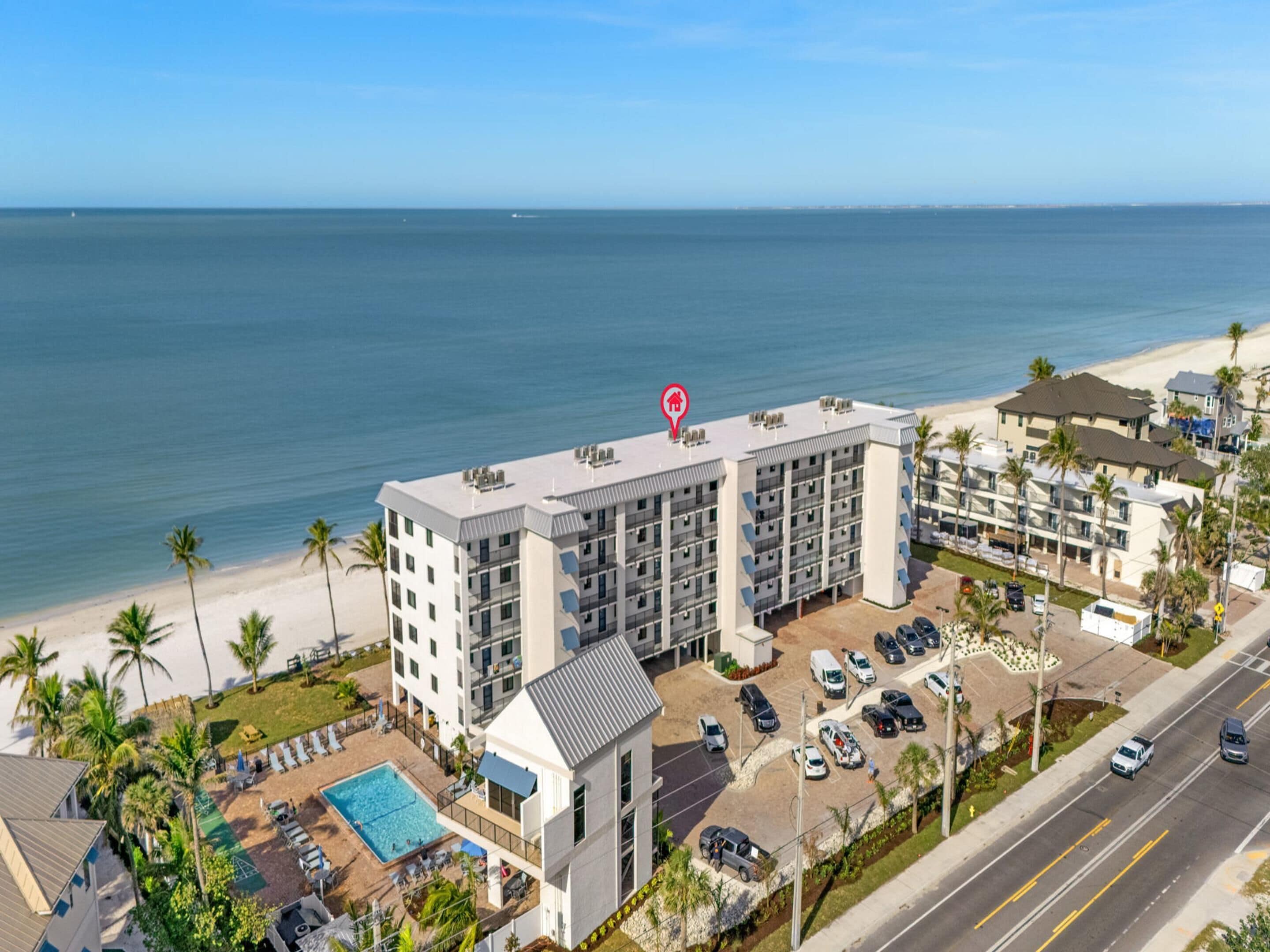 A multi-story hotel with a rooftop pool, adjacent to a beach and ocean view.