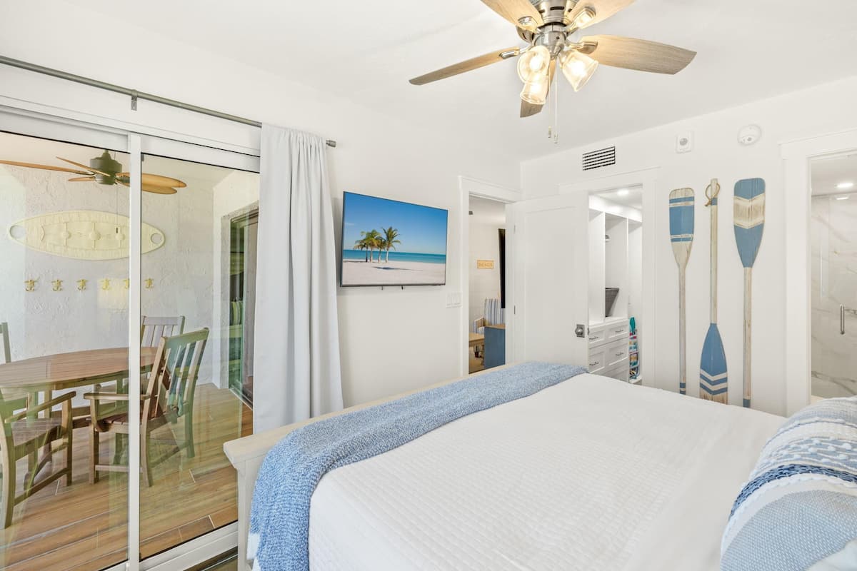 Quarto com cama, ventilador de teto, pintura de uma praia e dois pranchas de remo na parede.