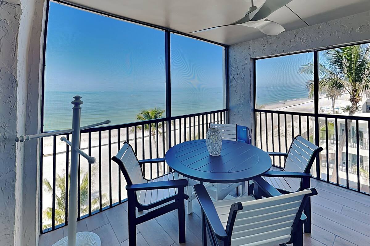 A balcony with a round table and chairs, a vase, and a view of the ocean.