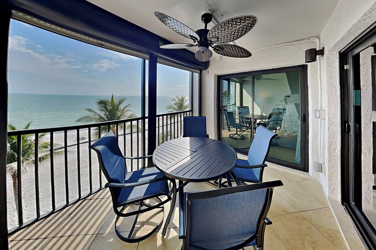 A balcony with a table and chairs, a ceiling fan, and a view of the ocean.