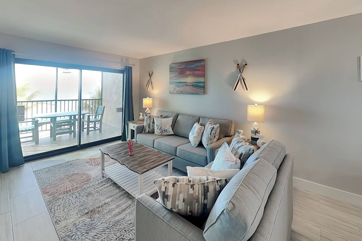 A living room with a sofa, coffee table, and a view of a balcony with outdoor furniture.