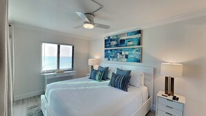 Ein modernes Schlafzimmer mit einem großen Bett, zwei Nachttischen mit Lampen, einem Deckenventilator und einem Fenster mit Jalousien.