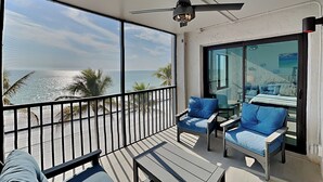 Ein Balkon mit Blick auf den Strand, zwei blaue Sitzgelegenheiten, ein kleiner Tisch und ein Deckenventilator.