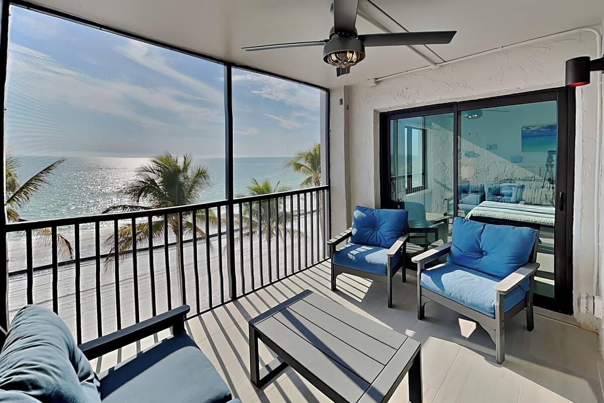 A balcony with a view of the ocean, furnished with blue chairs and a table.