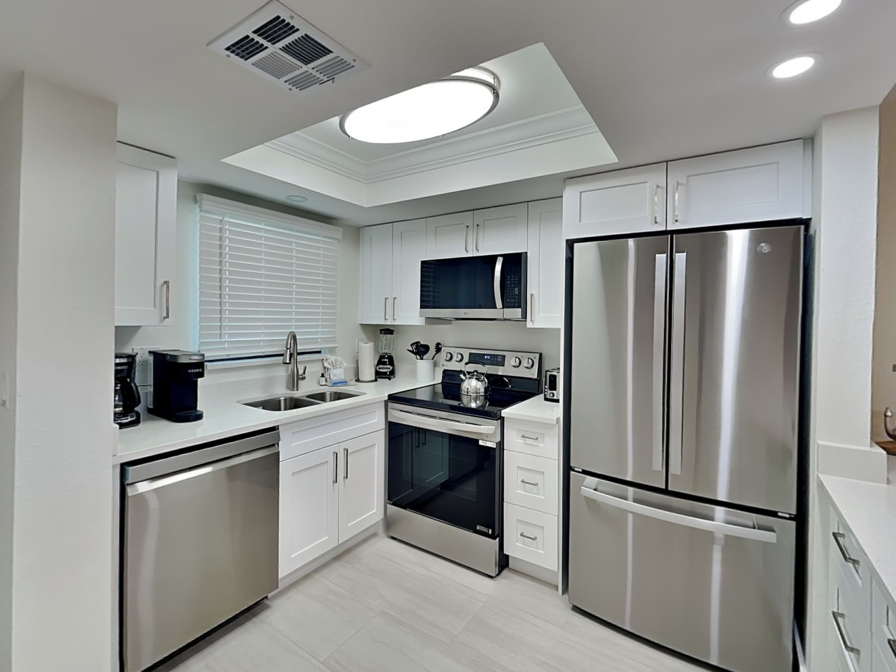 Una cocina moderna con armarios blancos, electrodomésticos de acero inoxidable, un microondas integrado y un refrigerador grande.