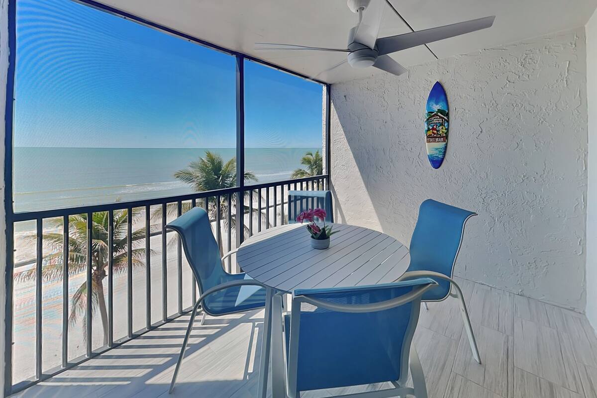 A balcony with a view of the beach, a ceiling fan, and a surfboard decoration.