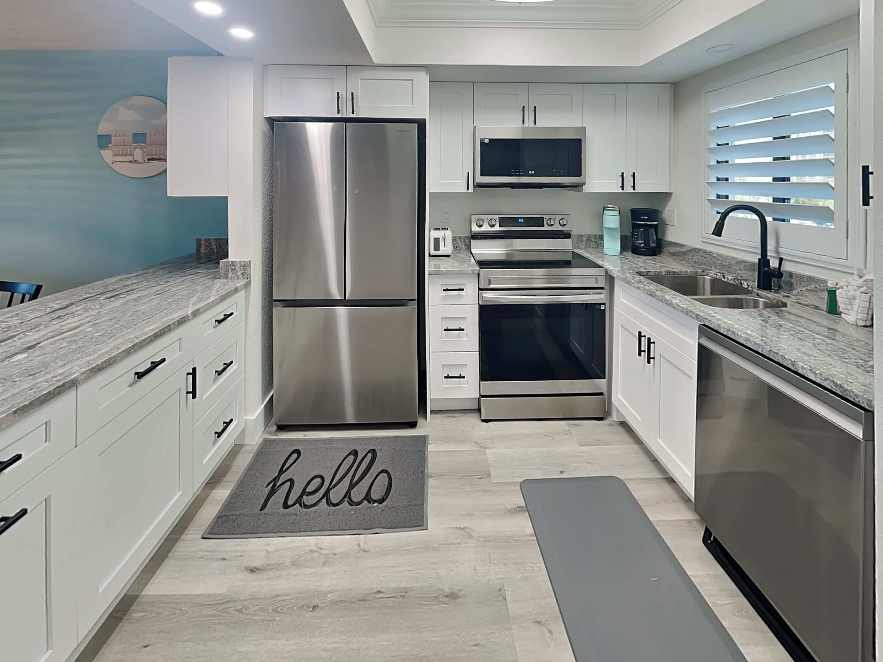 A modern kitchen with stainless steel appliances, white cabinetry, and a grey marble countertop.