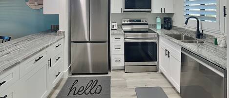 A modern kitchen with stainless steel appliances, white cabinetry, and a grey marble countertop.