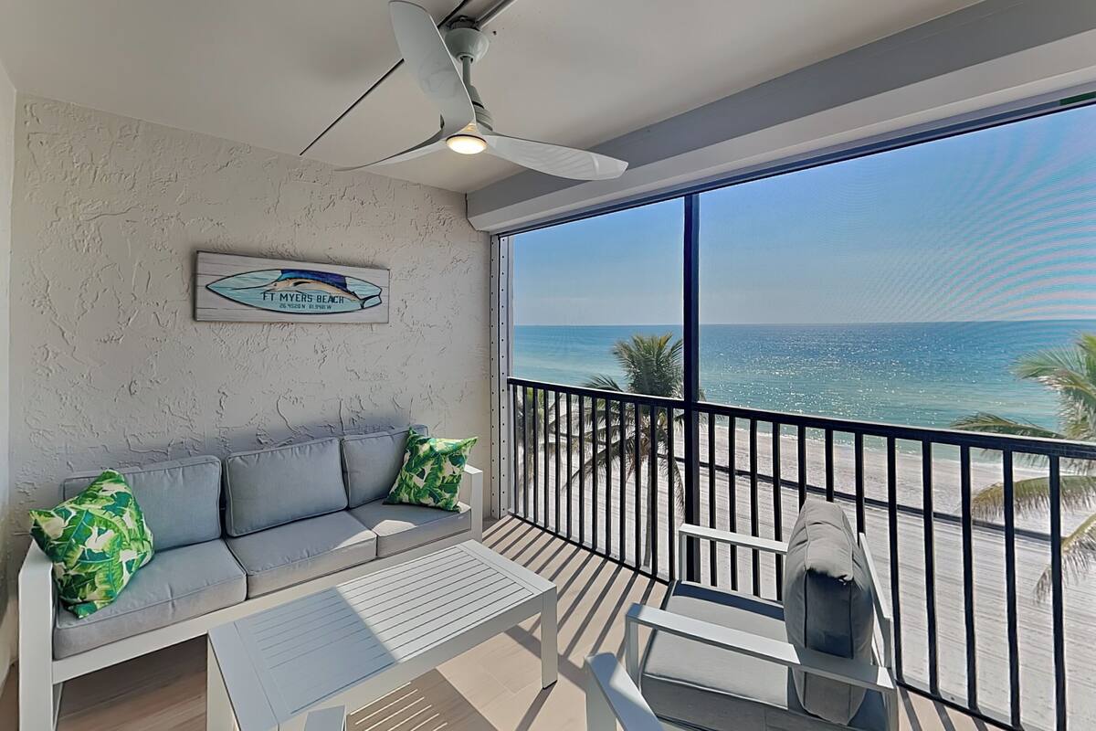 A balcony with a view of the ocean, a ceiling fan, a sofa with cushions, and a sign on the wall.