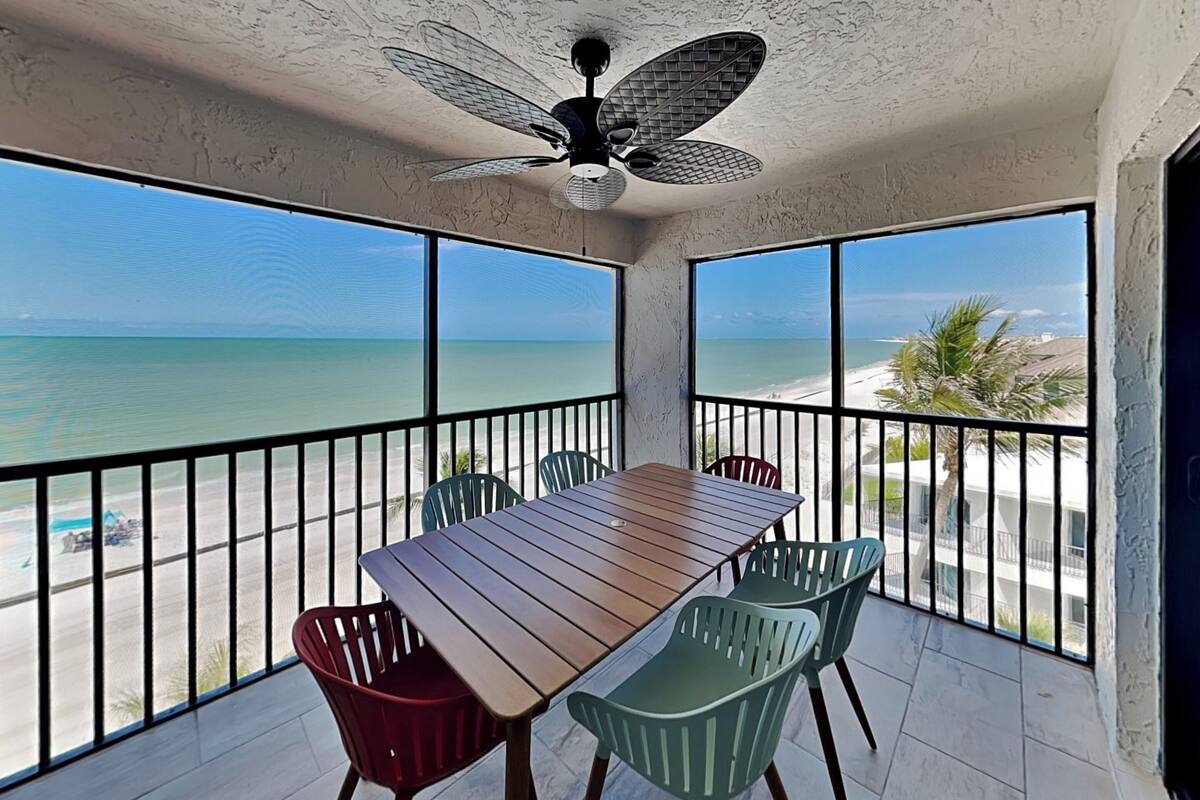 Un balcon avec une table et des chaises en bois, donnant sur une plage et l’océan.