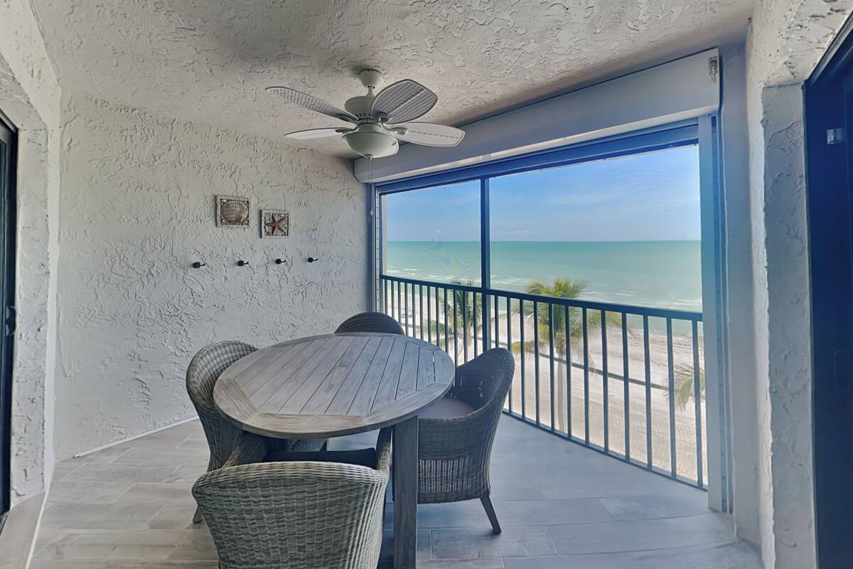 Un balcon avec vue sur la plage, une table ronde et des chaises en osier.