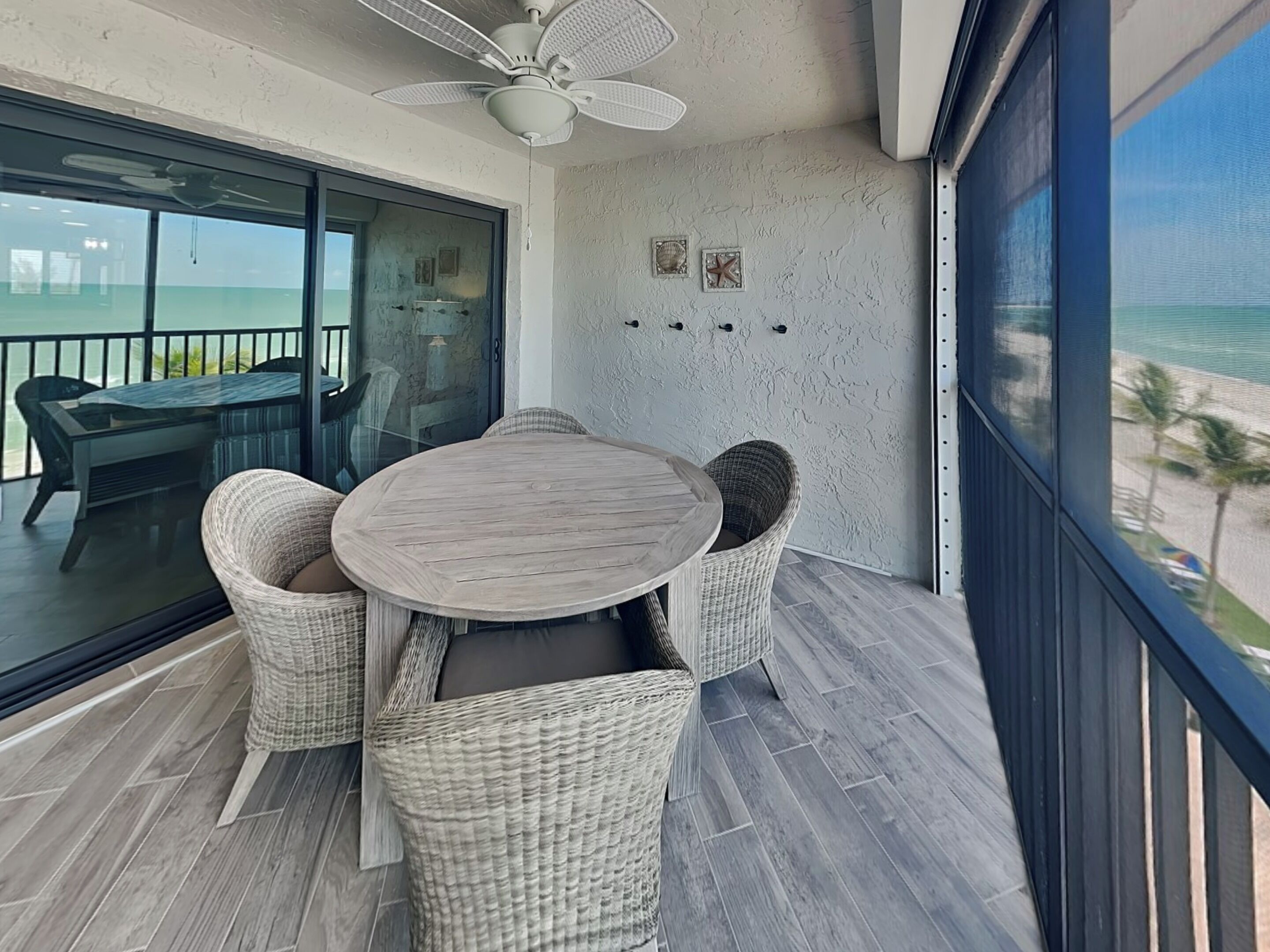 Ein Balkon mit rundem Tisch und Korbstühlen mit Blick auf einen Strand.
