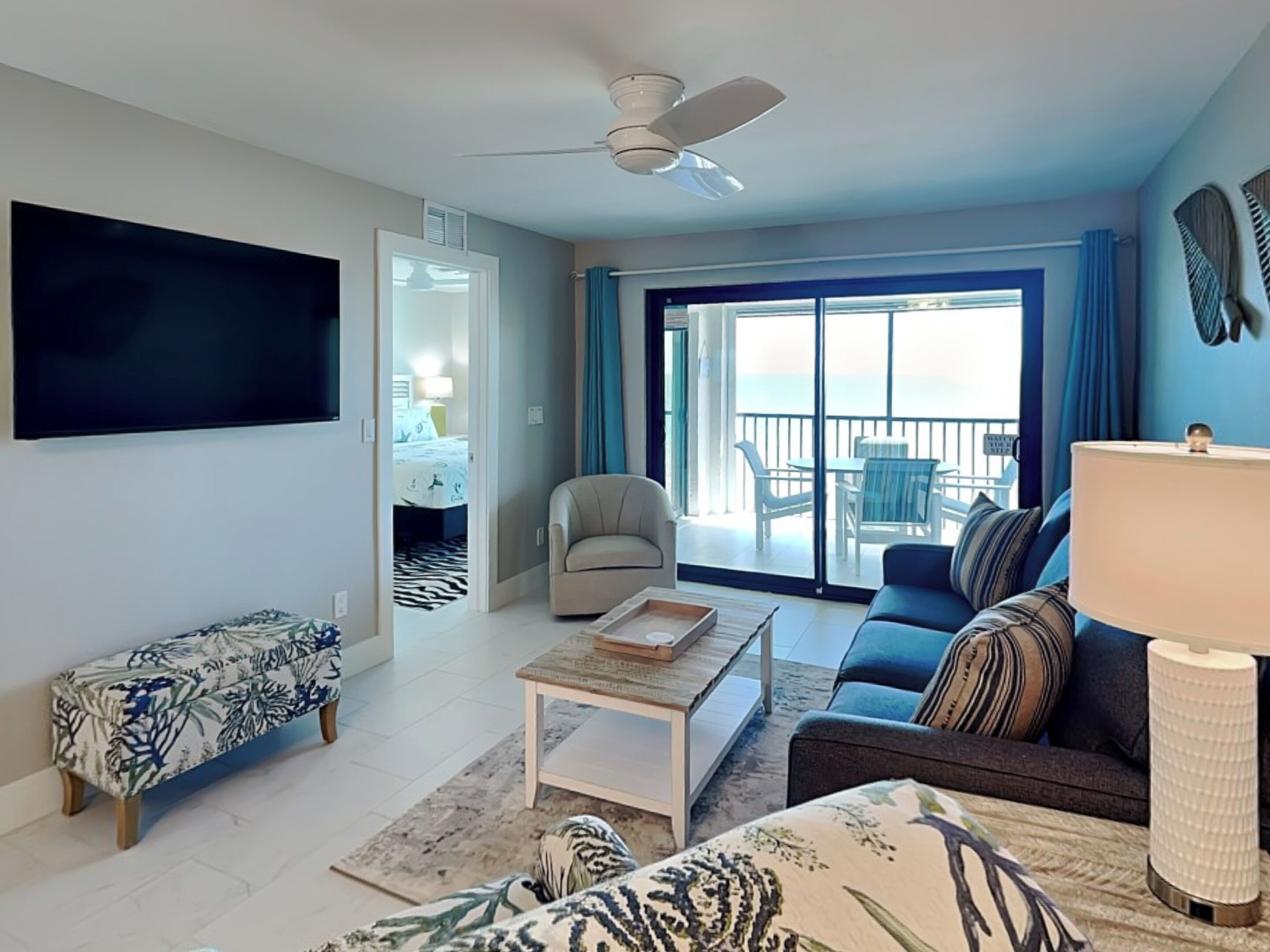 Ein modernes Wohnzimmer mit Flachbildfernseher, einer Couch, einem Couchtisch und einer Bank. Ein Balkon bietet Blick aufs Meer.