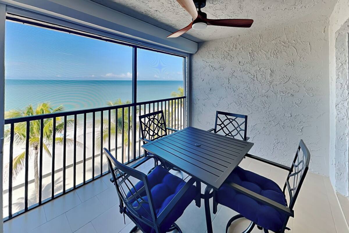 Un balcon avec une table et des chaises, un ventilateur de plafond et une vue sur l’océan.