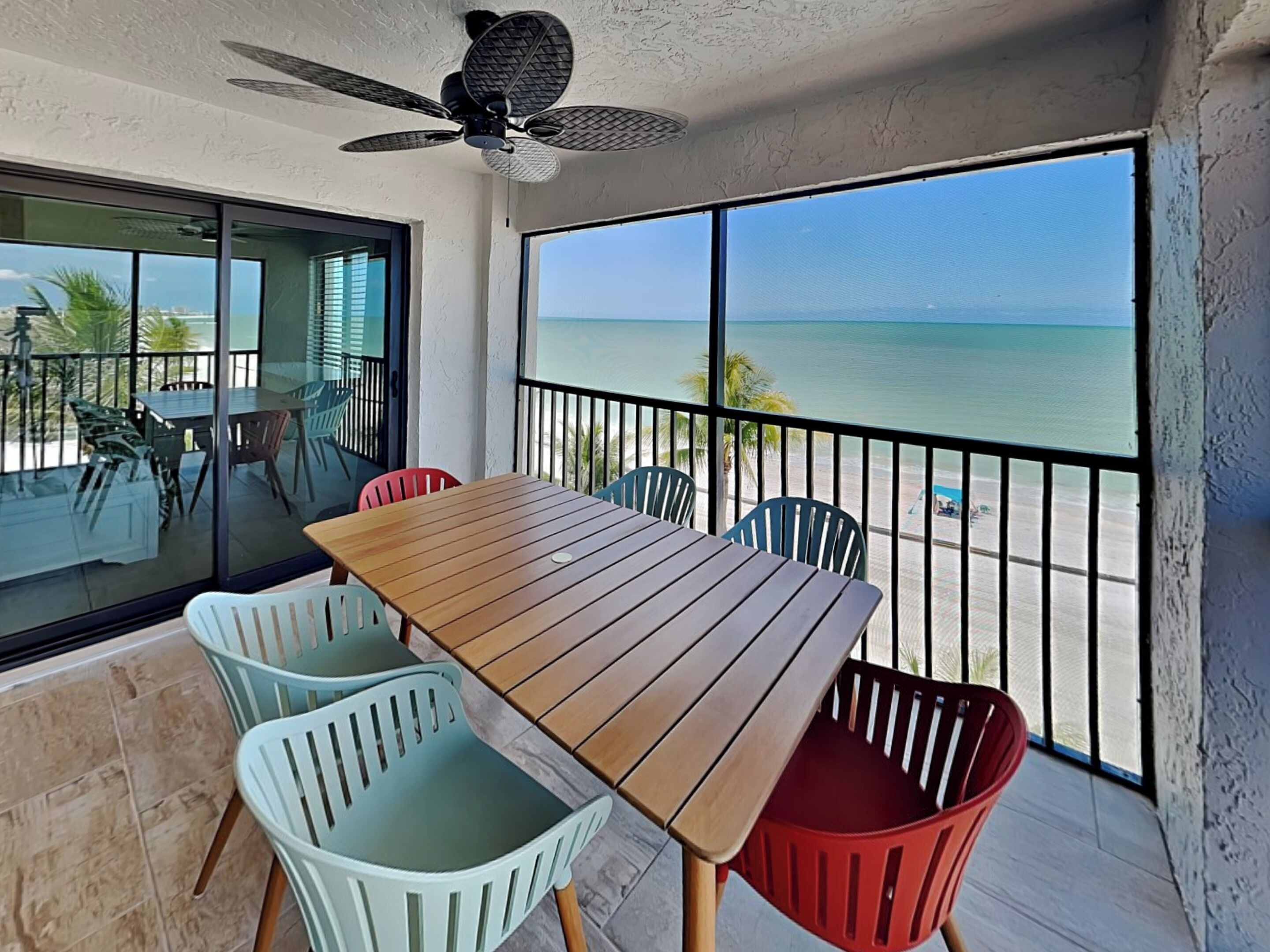 A balcony with a wooden table and chairs, a ceiling fan, and a view of the ocean.