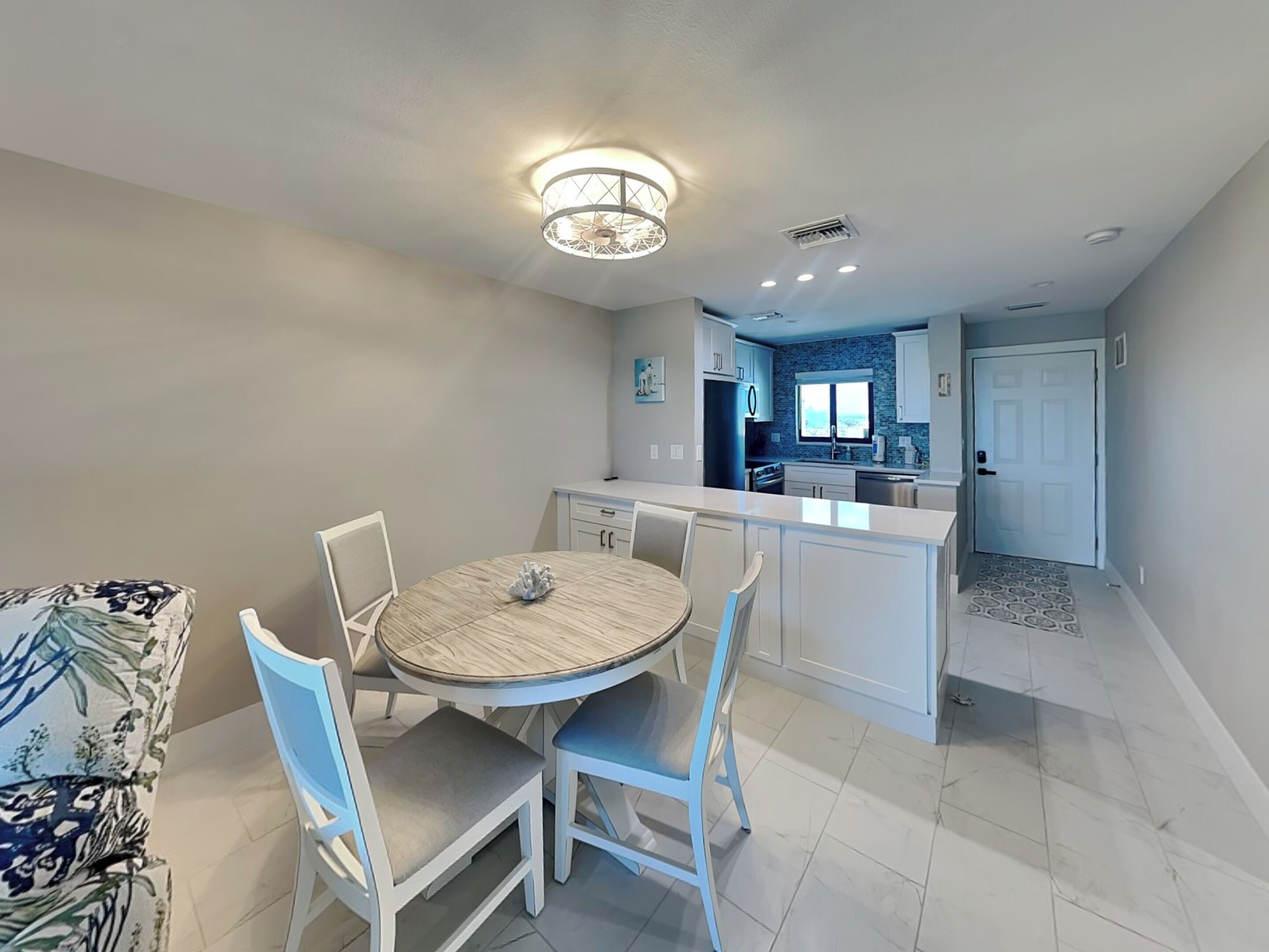 A modern kitchen with white cabinetry, a central island, and a dining area with a round table and chairs.