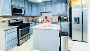 Cocina moderna con armarios azules, electrodomésticos de acero inoxidable, encimeras de granito y una isla central con frutero.
