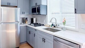 Una cocina moderna con gabinetes grises, electrodomésticos de acero inoxidable y un ventanal con persianas.