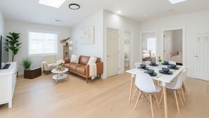 Una sala de estar moderna con un sofá de cuero marrón, una mesa de comedor blanca y una pequeña mesa de centro.