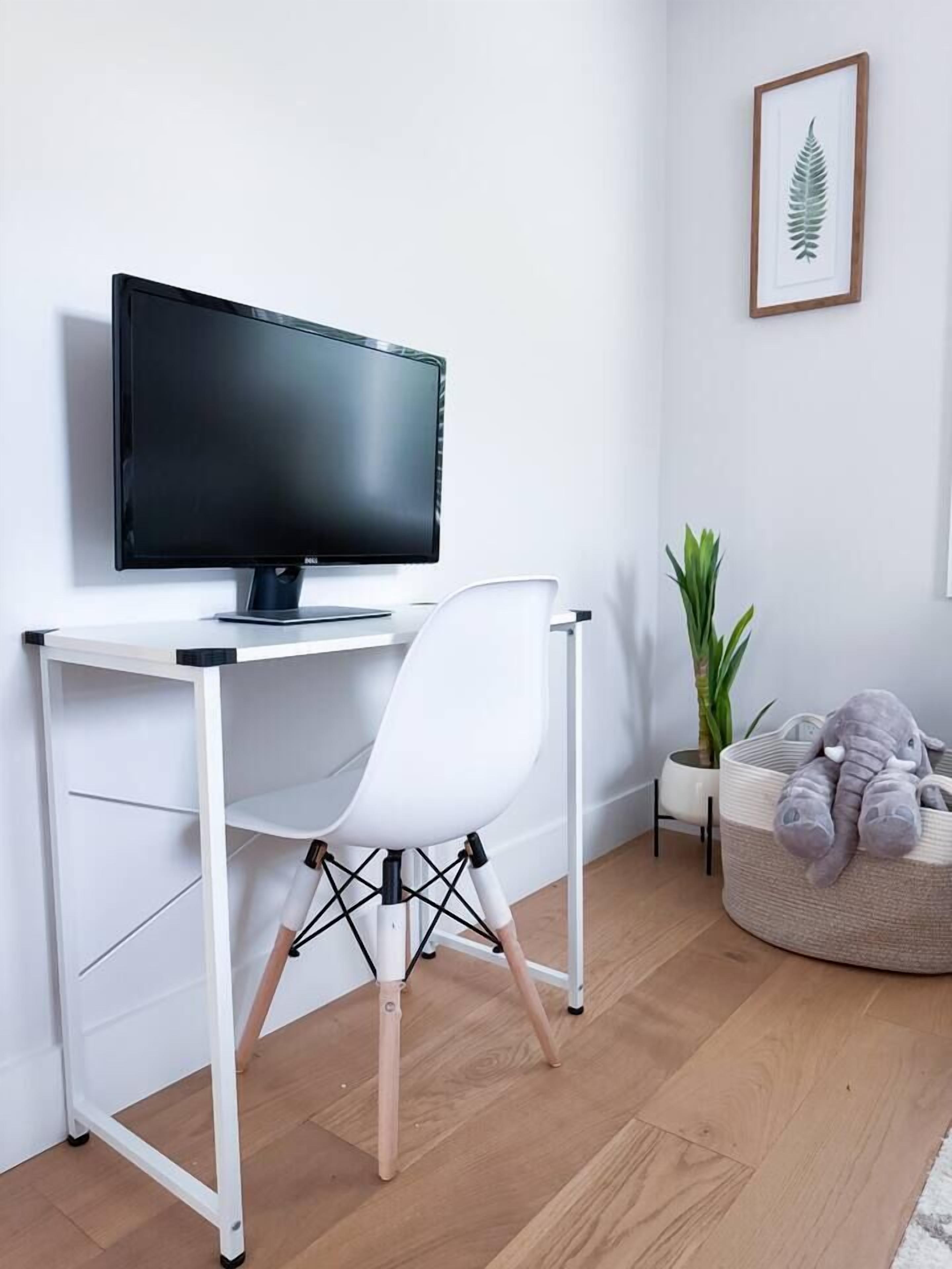 A white desk with a black monitor, a white chair, a small potted plant, and a bean bag chair with an elephant plush toy.
