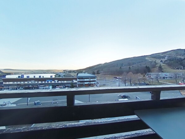 Vista desde un balcón sobre un estacionamiento con edificios y un paisaje montañoso al fondo.