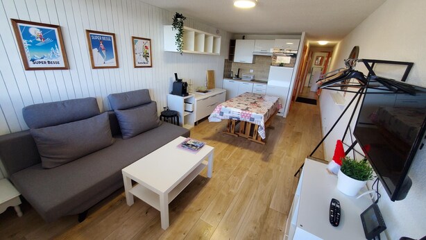 A compact living space with a sofa, a small dining table, a kitchenette, and a TV.