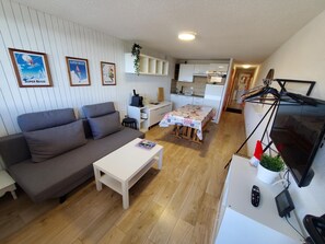 A compact living space with a sofa, a small dining table, a kitchenette, and a TV.