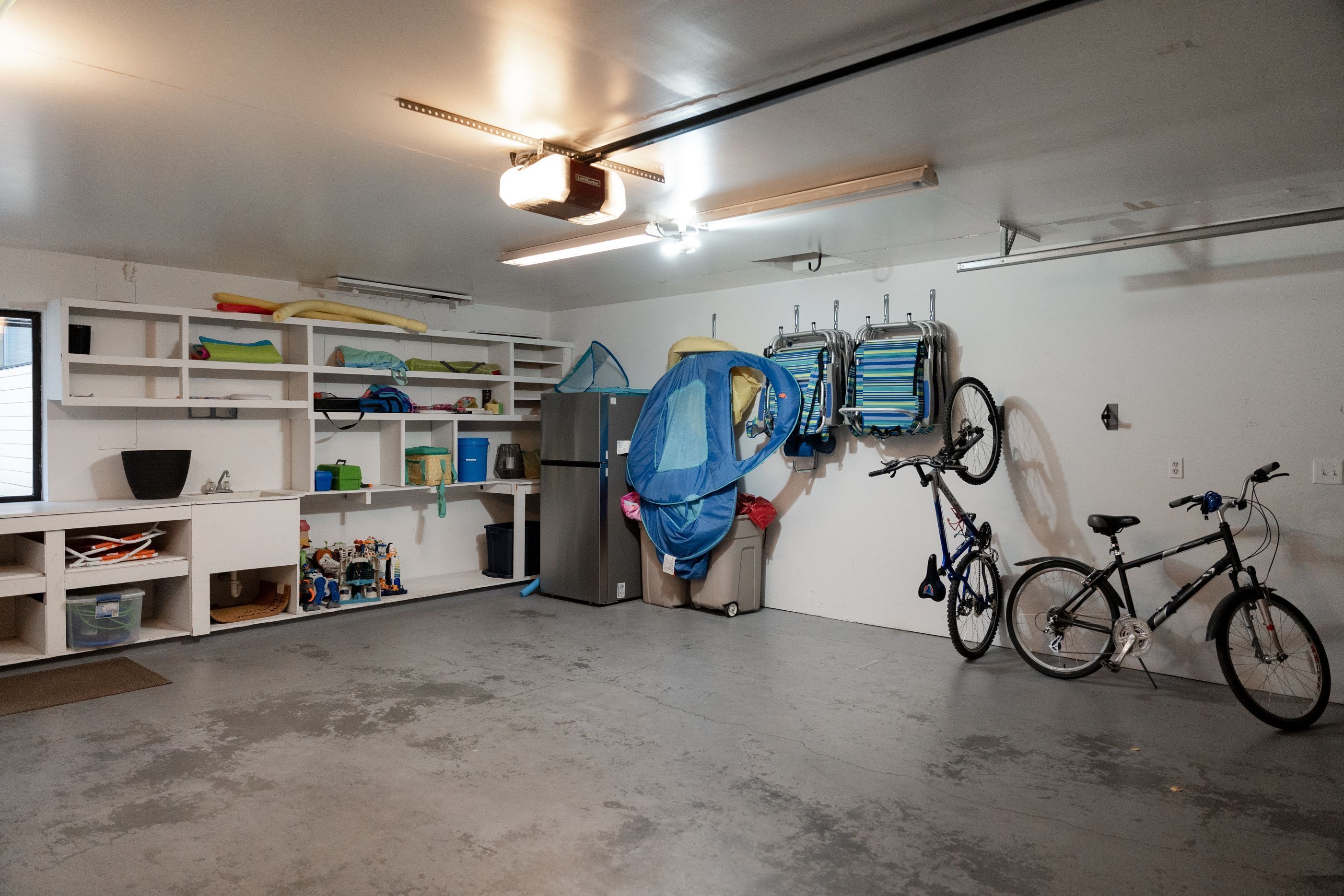 Eine Garage mit Deckenventilator, Regalen mit gefalteter Kleidung, einem Fahrrad und einem Kühlschrank.