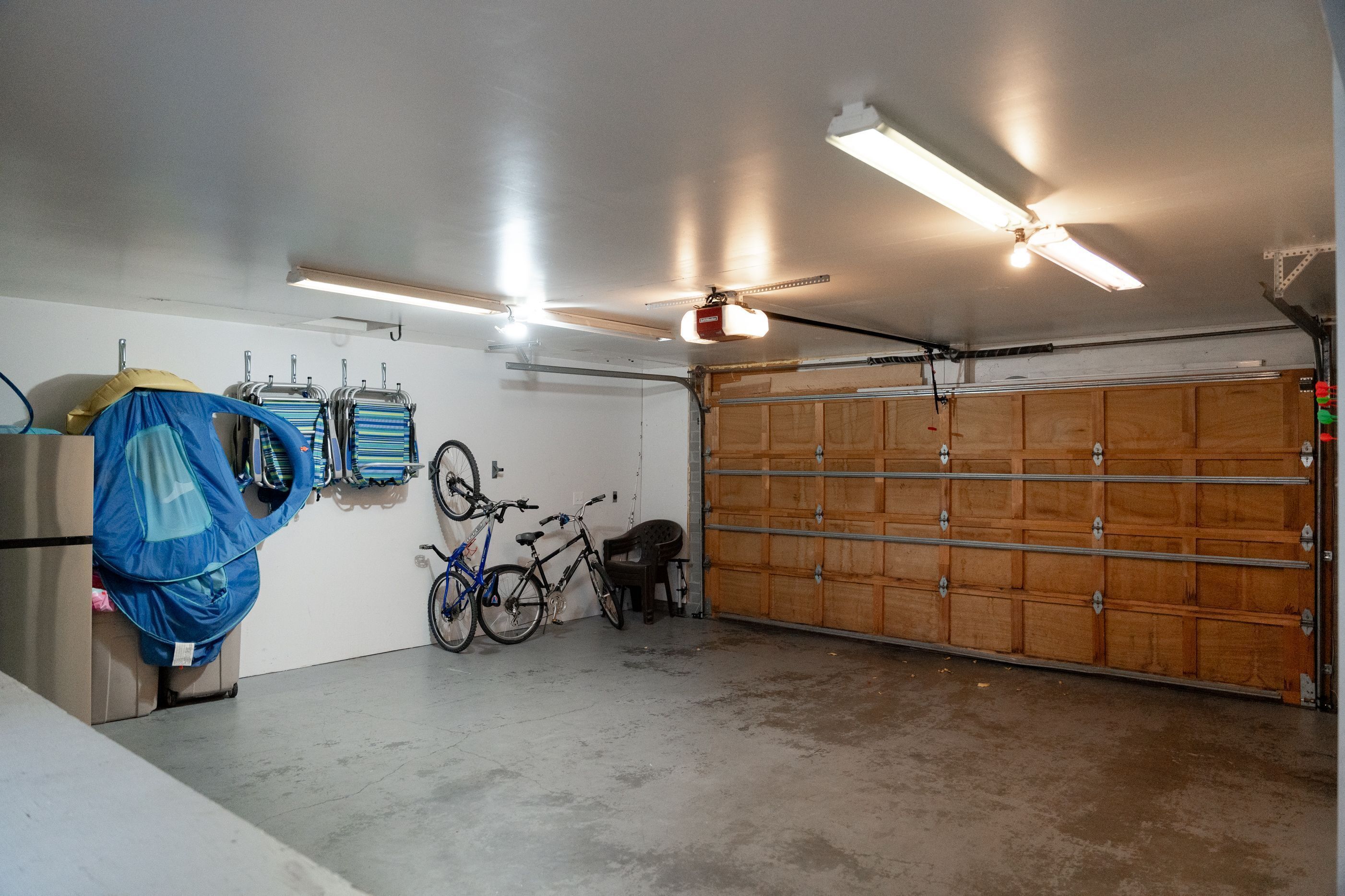 A garage with a wooden door, ceiling fans, fluorescent lights, and bicycles.