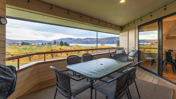 A balcony with a table and chairs, a clock, and a view of a vineyard and mountains. - Wapato Point Resort home with hot tub and views (Manson)