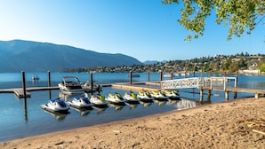 A lakeside dock with several jet skis and a boat, surrounded by calm water and distant mountains. - Wapato Point Resort home with hot tub and views (Manson)