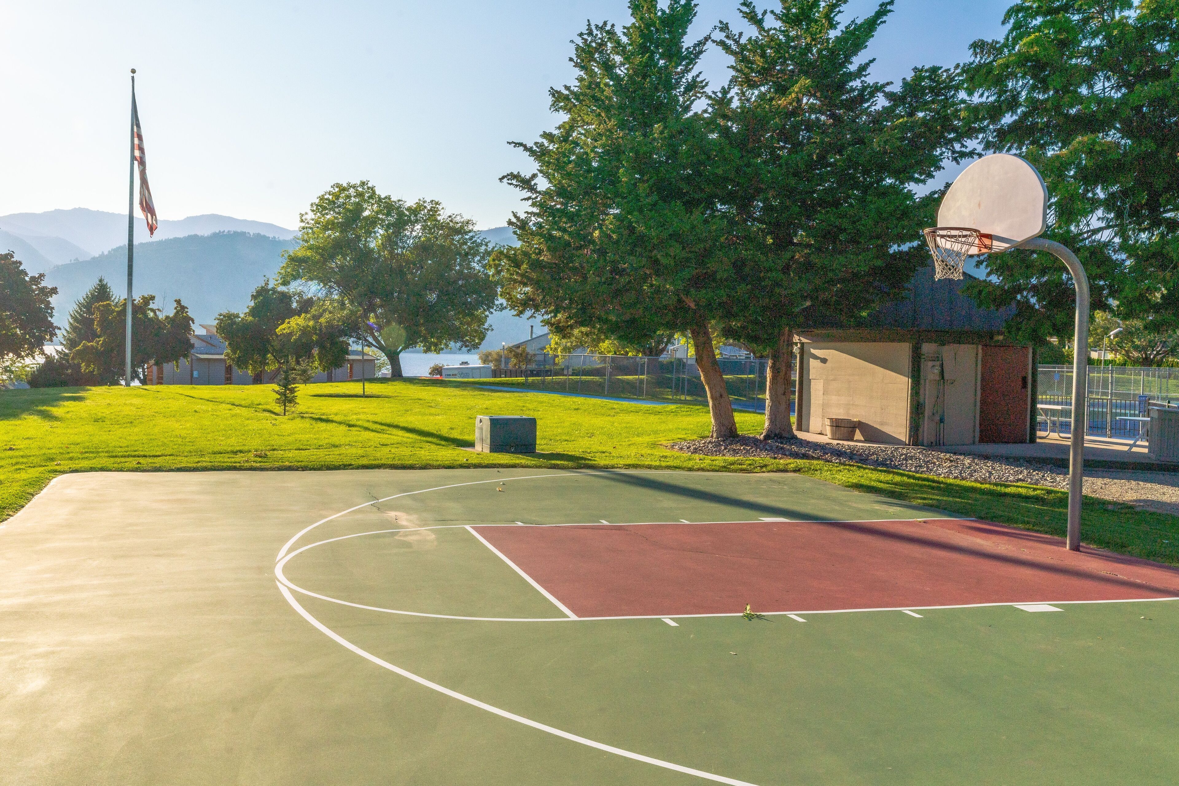 Un terrain de basket en plein air, avec un panier, entouré d’arbres et sous un ciel dégagé.