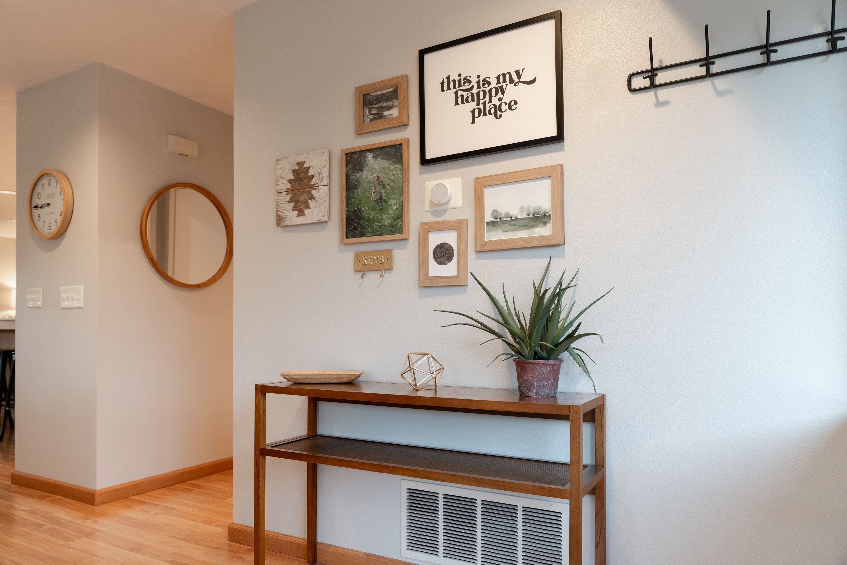 A hallway with a wooden console table, a potted plant, and various framed pictures on the wall.
