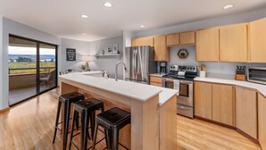 A modern kitchen with a large island, stainless steel appliances, wooden cabinets, and a view of a lake. - Wapato Point Resort home with hot tub and views (Manson)