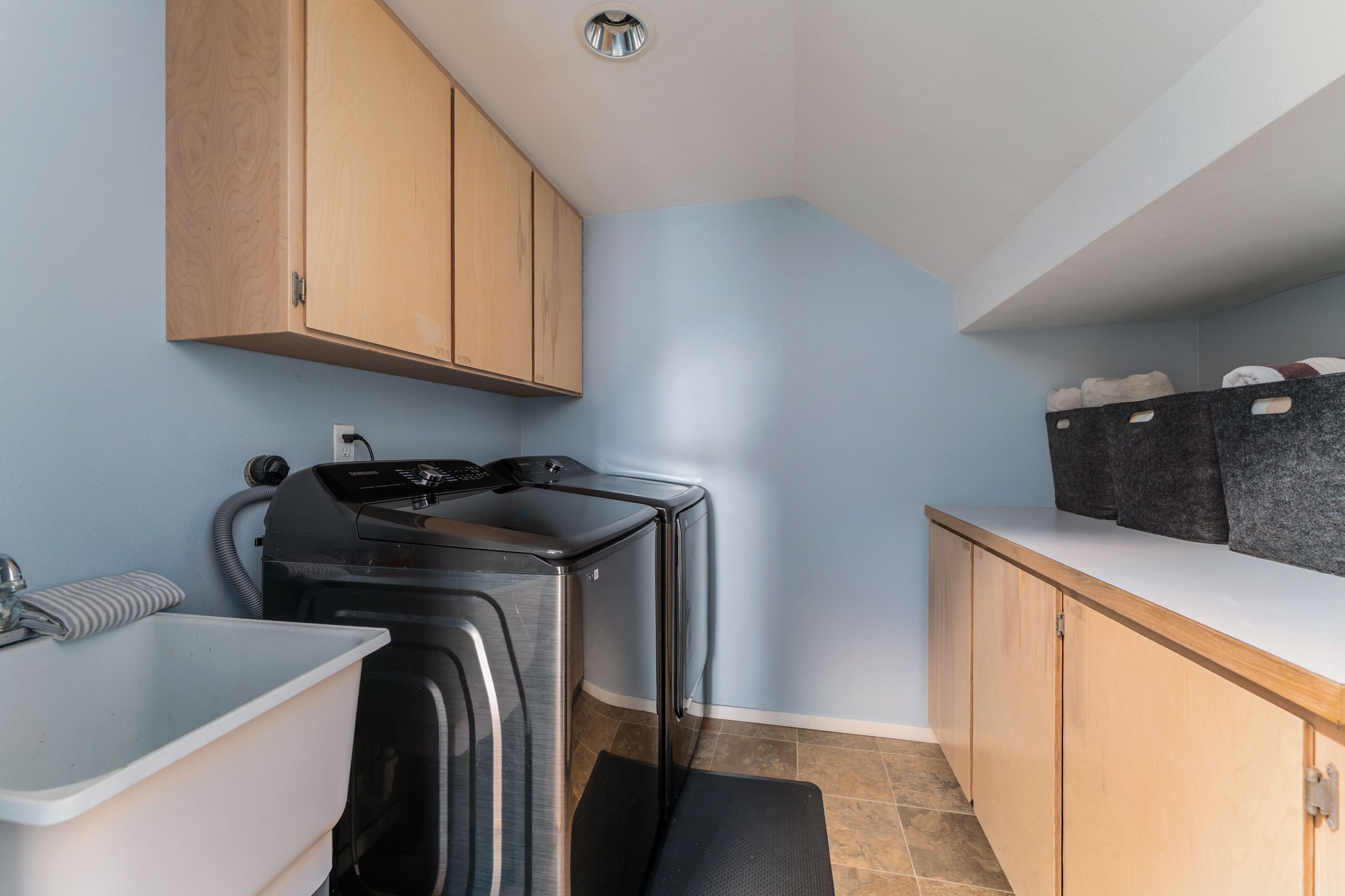 A compact kitchen with wooden cabinets, a built-in stove, a sink, and a countertop with storage baskets.