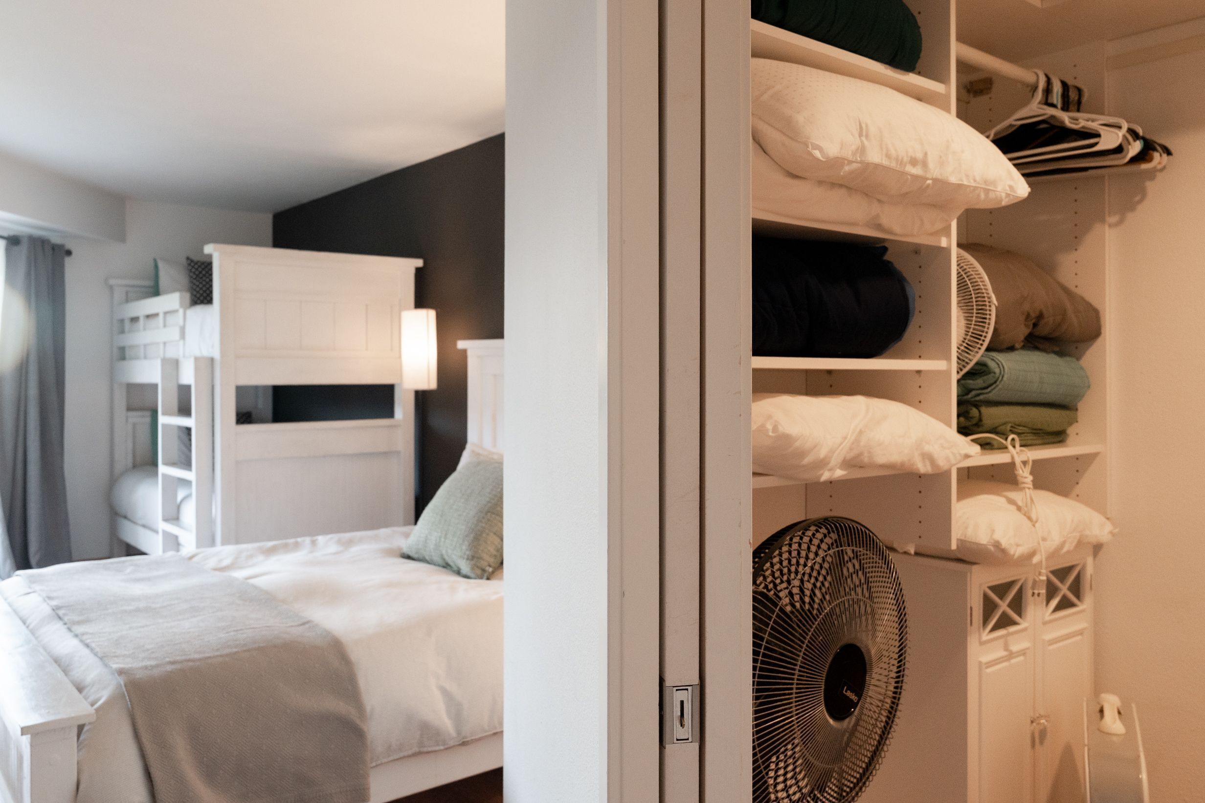 Un dormitorio con una cama individual doble, una mesita de noche, una lámpara y un armario con estantes y espacio para colgar.