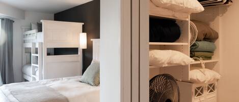 Un dormitorio con una cama individual doble, una mesita de noche, una lámpara y un armario con estantes y espacio para colgar.