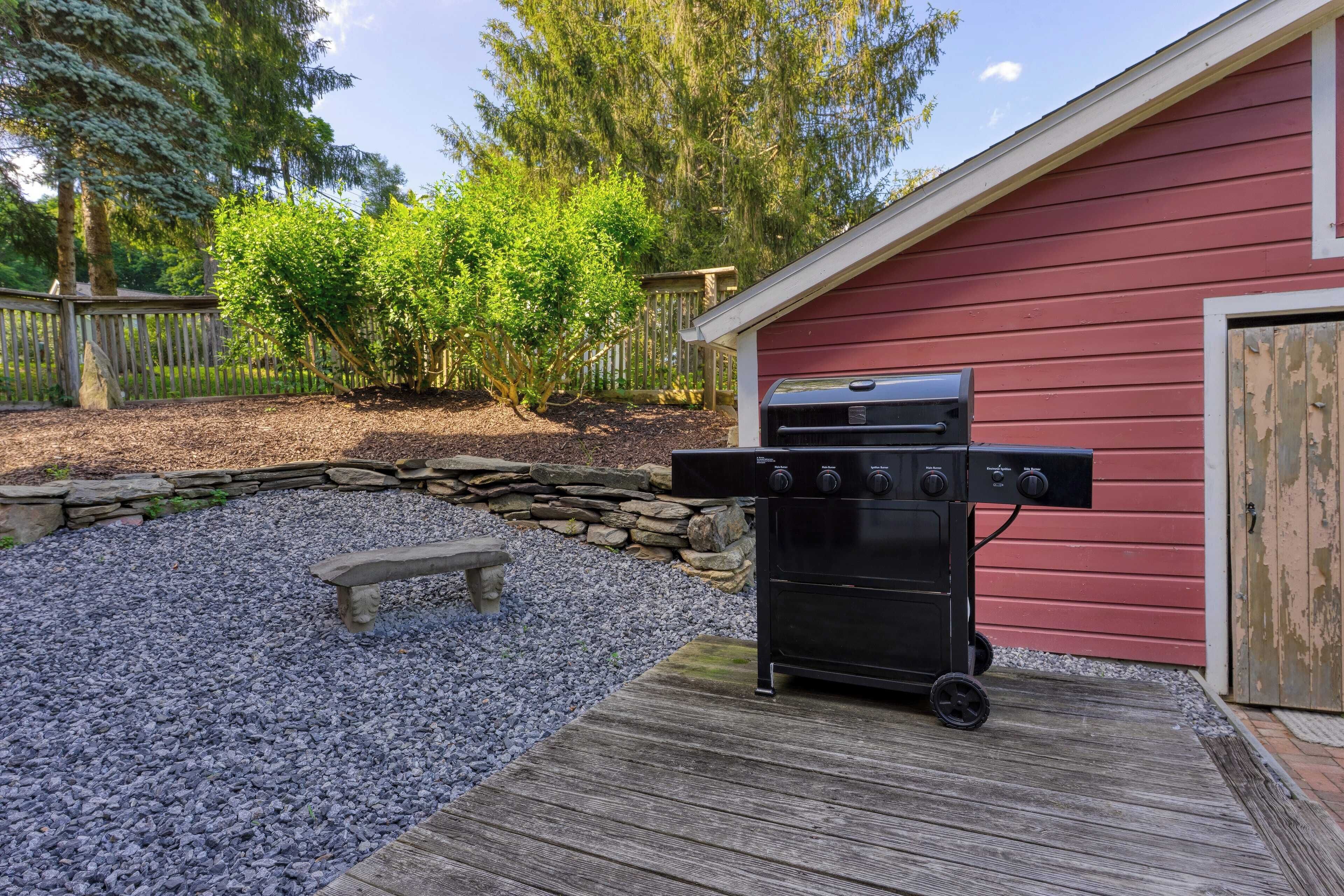 Un barbecue dans un jardin, avec un mur en pierre, une terrasse en bois et un bâtiment rouge.
