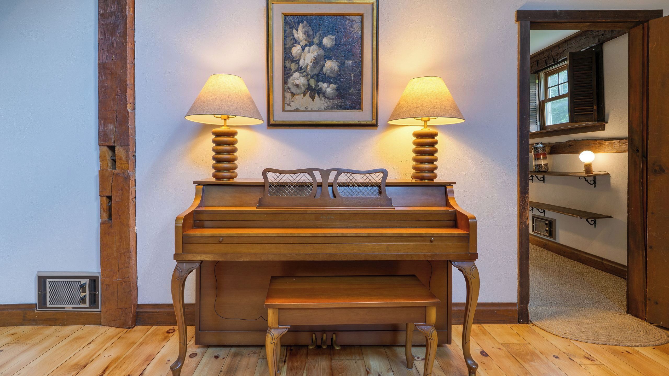Ein Holzpiano mit zwei Lampen, einem gerahmten Gemälde und einer hölzernen Bank.
