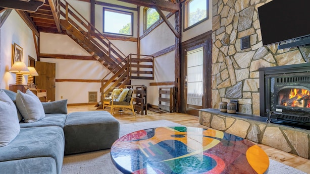 A cozy living room with a stone fireplace, a colorful glass coffee table, and a grey sofa. - Historic Barn Retreat w/ Pool & Pond Views Longview Pond Lodge by Avantstay (Clinton Corners)