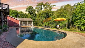 Una piscina con solárium, sillas de descanso y una zona de estar cubierta.