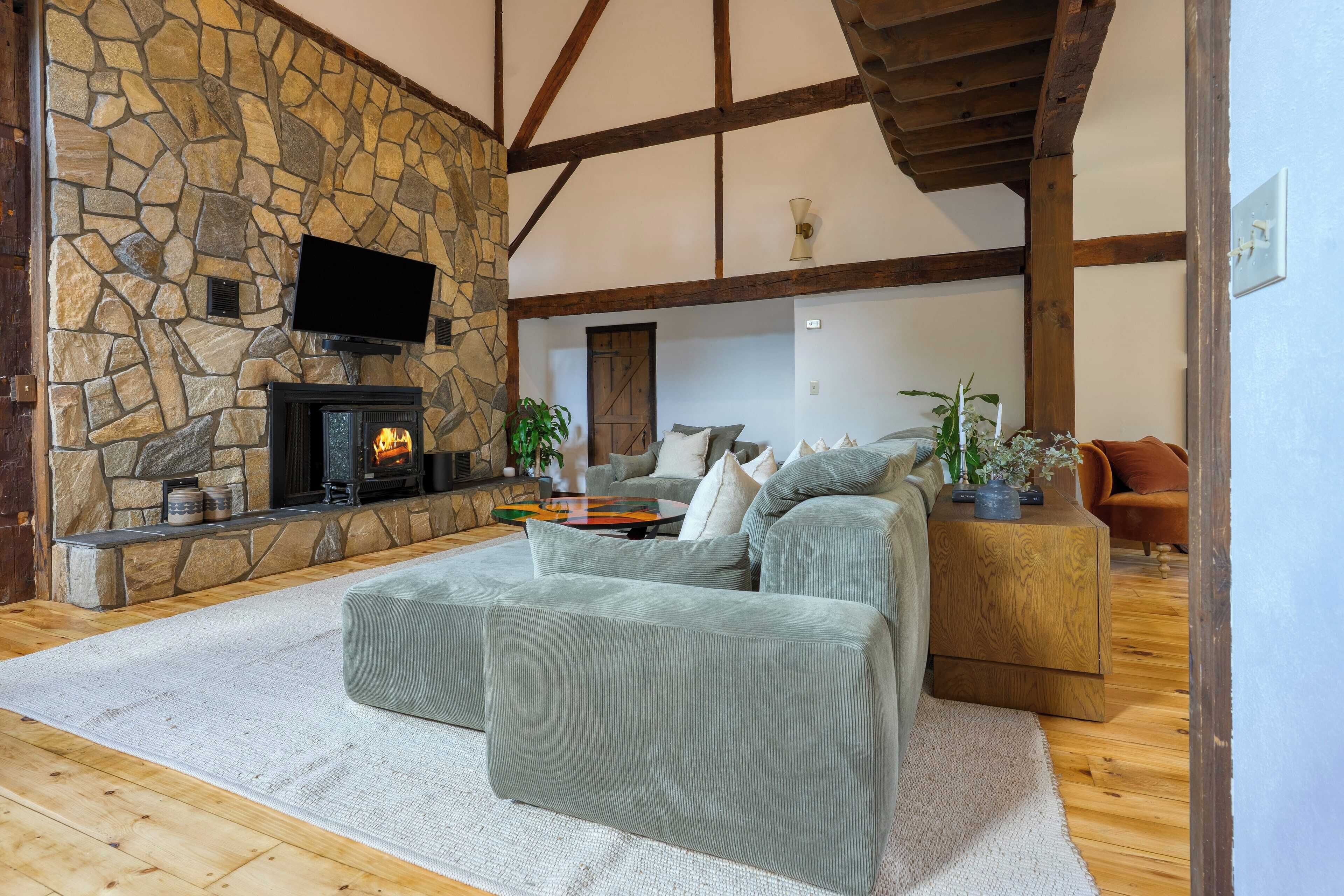 A cozy living room with a stone fireplace, a flat-screen TV mounted above it, and a comfortable seating area with a sofa and ottoman.
