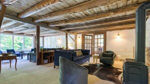 A rustic interior with exposed wooden beams, a sofa, a chair, a table, and a fireplace. - Historic Barn Retreat w/ Pool & Pond Views Longview Pond Lodge by Avantstay (Clinton Corners)