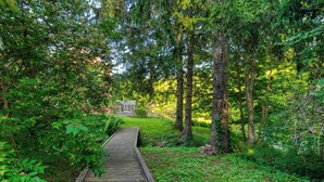 A wooden boardwalk through a forested area with a house in the background. - Historic Barn Retreat w/ Pool & Pond Views Longview Pond Lodge by Avantstay (Clinton Corners)