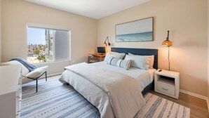 A bedroom with a large bed, a desk, a chair, a window with a view, and a painting on the wall. - NEW LUX Modern Retreat  Views  Parking  Workspaces (San Diego)
