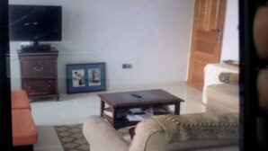 A living room with a sofa, a coffee table, a television, and a small cabinet. - Cameroon Comfort 2-bedroom apartment in peaceful Yassa with WiFi, AC, EspaceVert (Yassa)