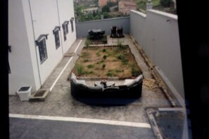 A rooftop with a small garden area, a white wall with windows, and a metal staircase. - Cameroon Comfort 2-bedroom apartment in peaceful Yassa with WiFi, AC, EspaceVert (Yassa)